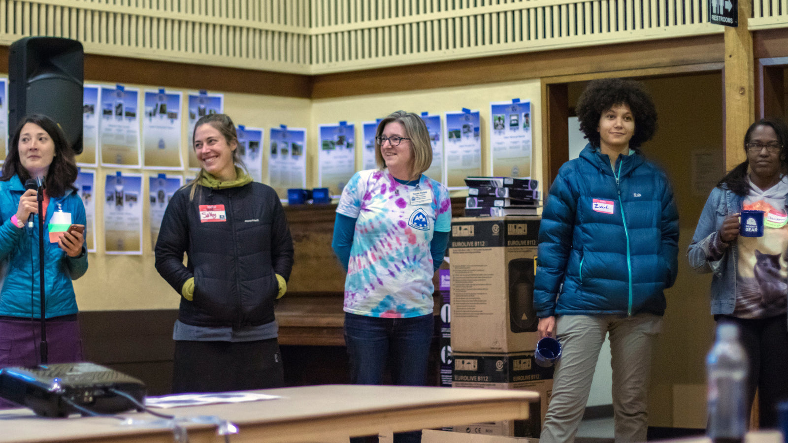 five women with trail name tags standing. One holds a microphone.